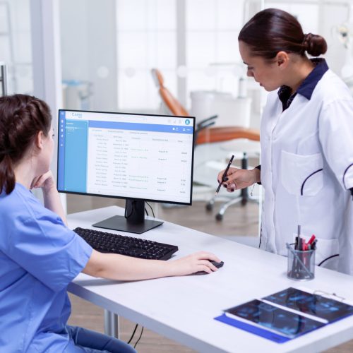 Stomatolog and nurse in tooth clinic checking patient appointment. Stomatolog and nurse in tooth clinic checking patient appointment looking at computer monitor. Stomatology assistant and teeth doctor discussing in reception of dental office